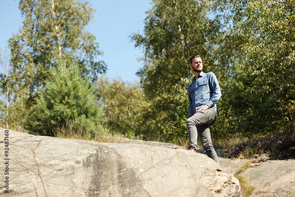 Attractive man wearing a jeans shirt and jeans, standing on top of a mountain looking forward, on a sunny summer day.