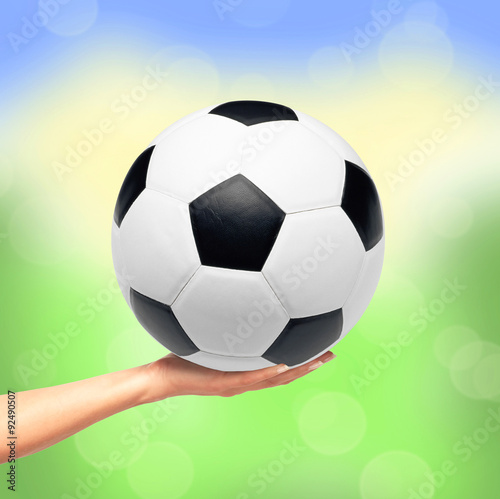 Hand holding soccer ball over bright nature background