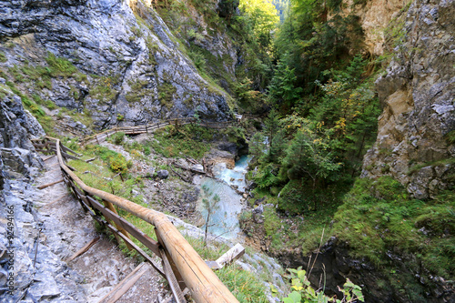 Waterfall cascading next to a narrow path along steep rocky walls at Wolfsklamm Gorge during Autumn in Stans, Austria  photo