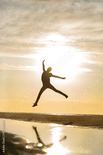 Young jumping girl silhouette in rays of sunlight at sunset.
