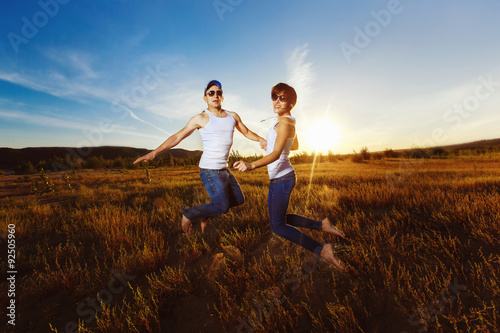 Young happy couple is jumping for joy at golden summer field 