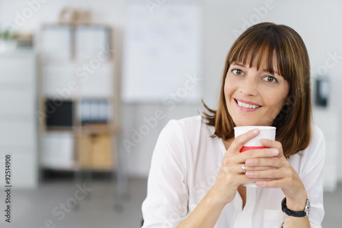 entspannte geschäftsfrau sitzt am schreibtisch mit einem becher kaffee