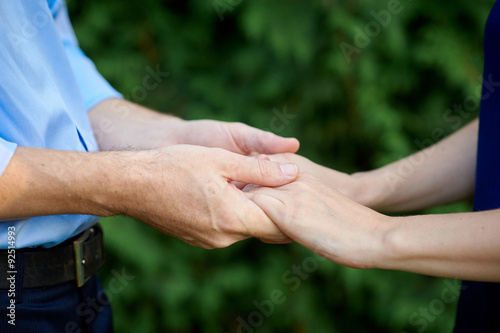 man holding a woman's hands on a background of green leaves