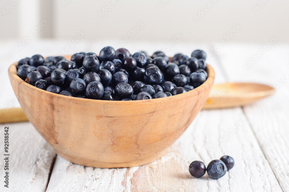 Wooden bowl with forest blueberry on white wooden background Wooden bowl with forest blueberry on white wooden background