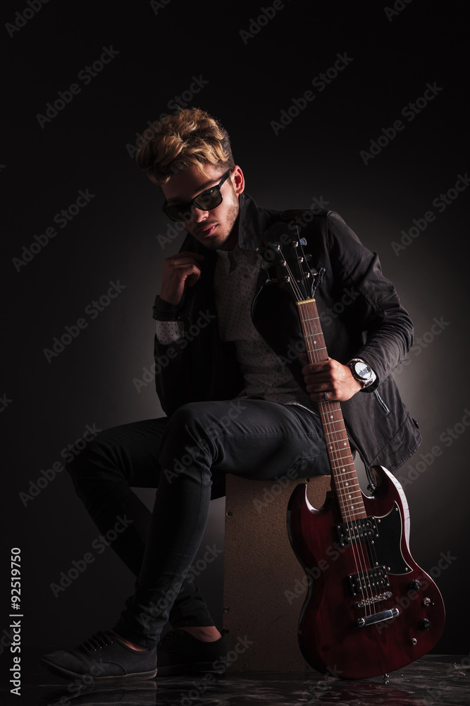 young guitarist sitting and holding his jacket by it's collar