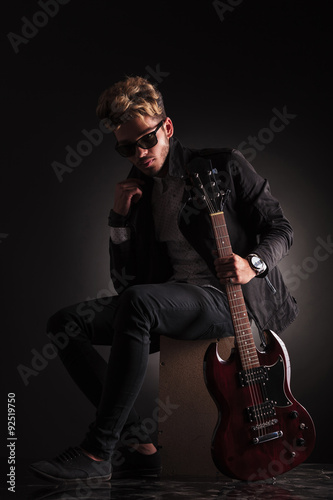 young guitarist sitting and holding his jacket by it's collar