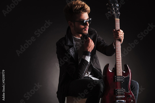 side of a cool guitarist sitting and holding his  guitar