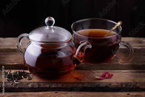 Glass teapot and cup with tea on wooden background dark still life