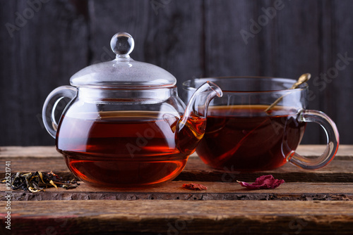 Glass teapot and cup with hot tea on wooden background dark still life