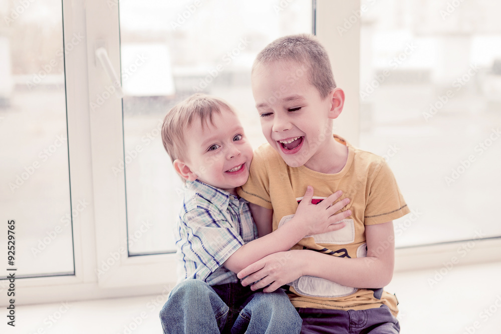 two boys laugh by playing. two happy brothers hugging each other and laughing together having fun sitting on the windowsill two boys laugh by playing. two happy brothers hugging each other and laughing together having fun sitting on the windowsill