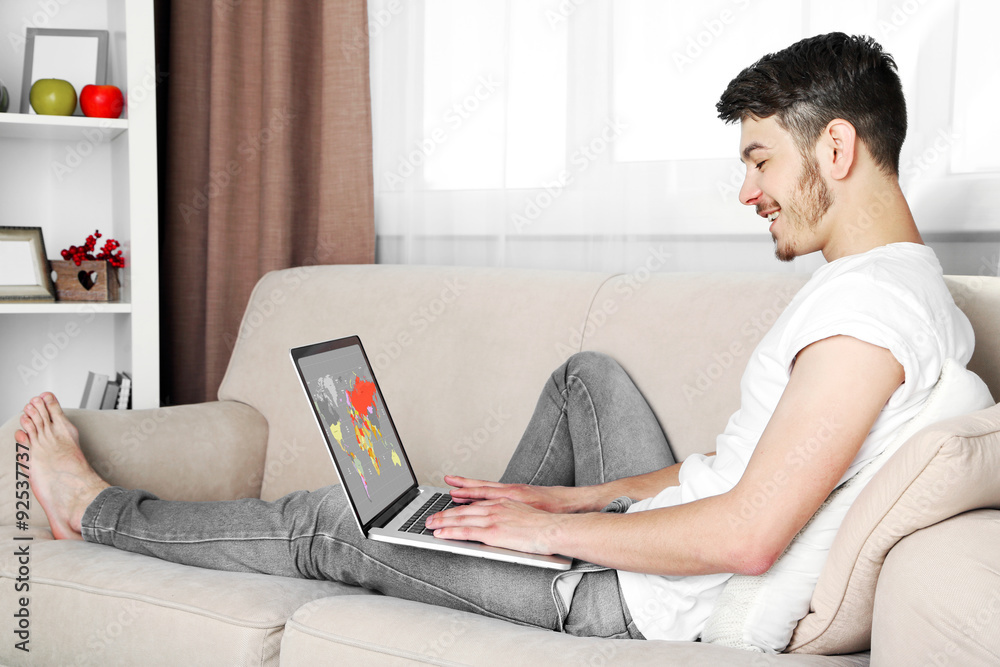 Handsome young man sitting on sofa and using laptop in room Handsome young man sitting on sofa and using laptop in room