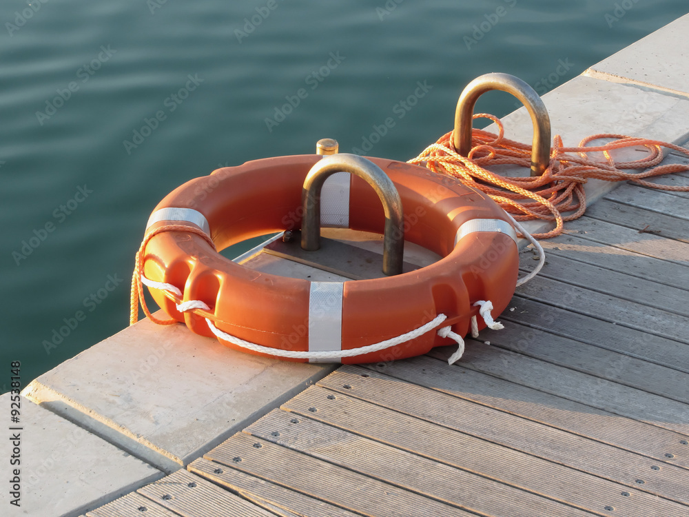 Fototapeta premium Orange life buoy on wooden pier in the harbor in Marina di Pisa, Tuscany, Italy
