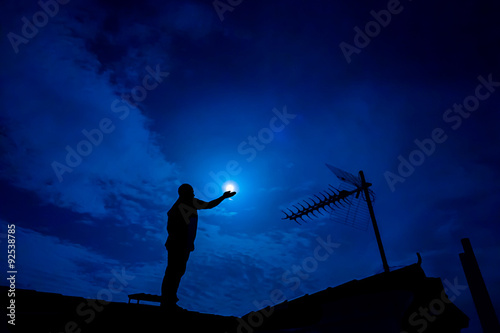 Man up on the roof, holding full moon in hand against night sky