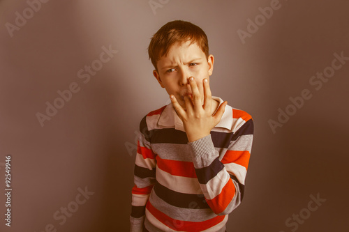 European-looking boy of ten years licks his finger on a gray bac