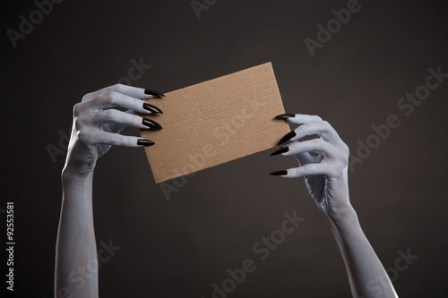 White witch hands with black nails holding blank cardboard