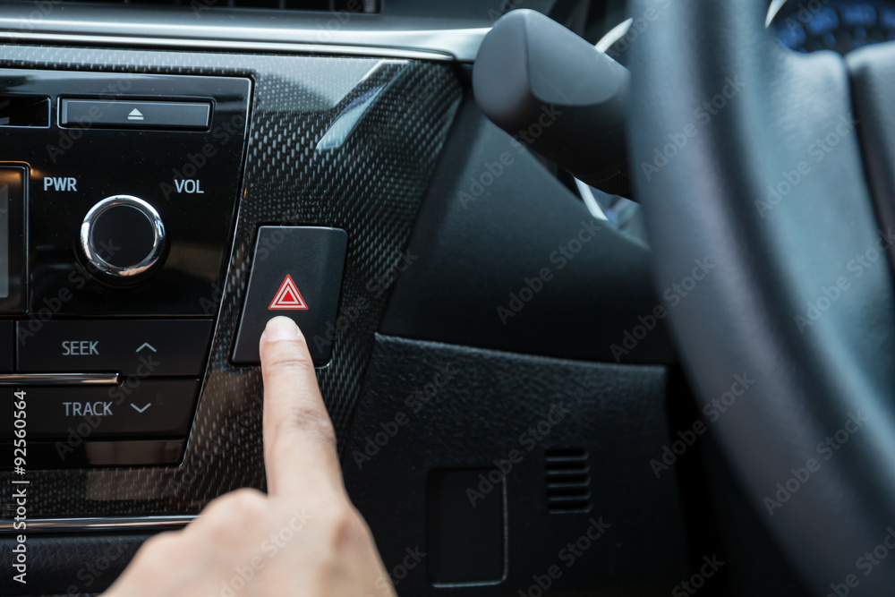 Closeup of young woman pressing emergency button on car sport dashboard.