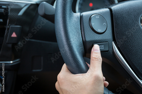 A woman hand pushes the mode hold control button on a steering wheel. © powerbeephoto