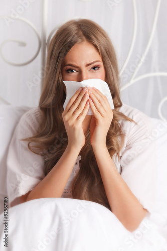Sick woman blowing her nose in the bed
