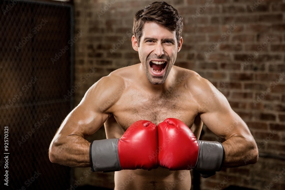 Shirtless man smiling while wearing boxing gloves