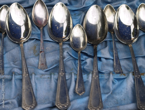 Group of aged dirty spoons lying on a dirty blue cloth (flea market)