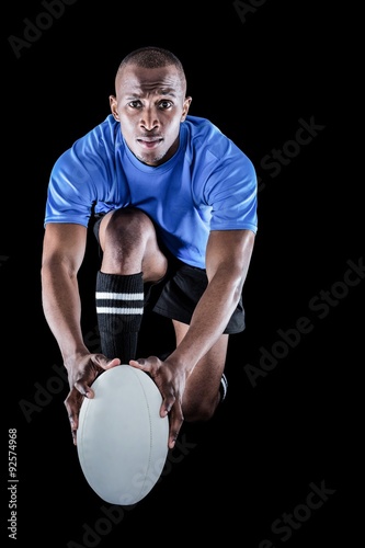 Portrait of rugby player kneeling and holding ball