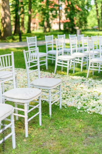 White wedding chairs set up and petals on green grass before the ceremony