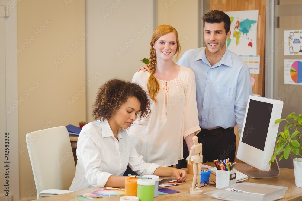 Business people standing by colleague working at desk Business people standing by colleague working at desk