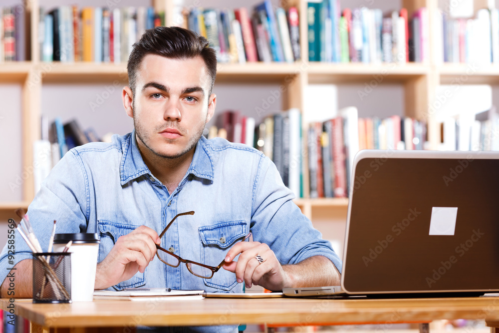 Fototapeta premium Serious young man sitting at the table with laptop
