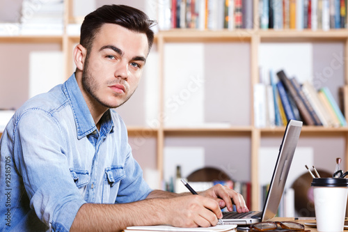 Close up view of young handsome man, sitting with laptop