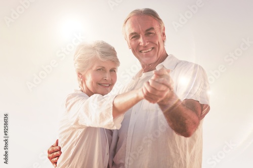 Composite image of senior couple dancing on the beach