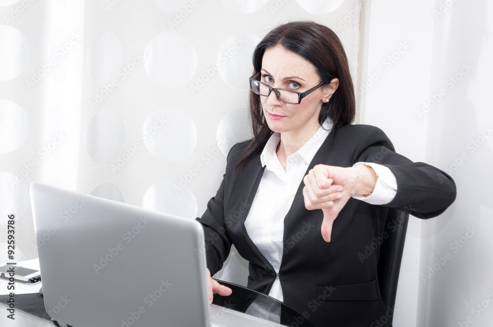 Woman working in a office shows the thumbs down gesture expressing her dissatisfaction with a project shown on the computer Woman working in a office shows the thumbs down gesture expressing her dissatisfaction with a project shown on the computer
