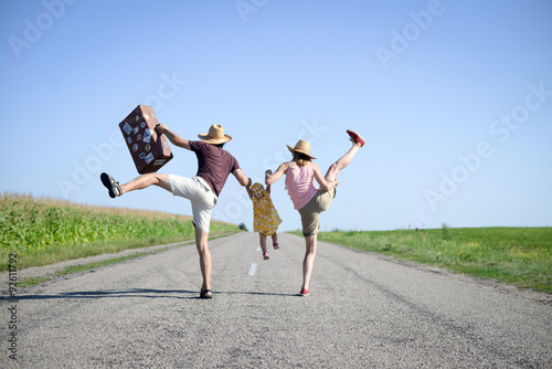 Parents and baby with suitcase jumping and dancing on road