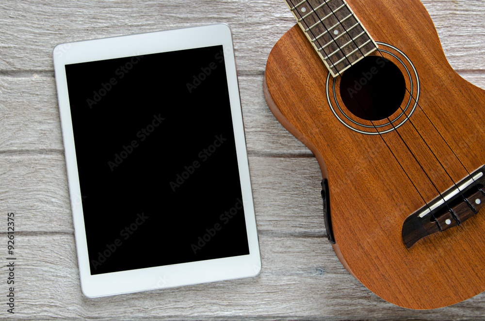 Fototapeta premium tablet and ukulele guitar on white wooden table
