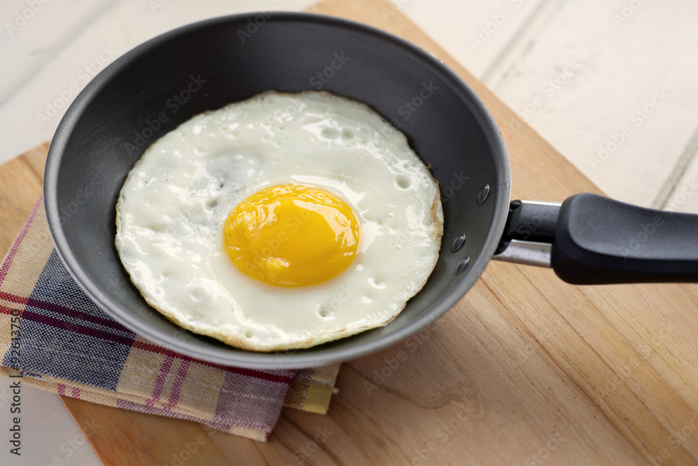 Fried egg in pan. Fried egg inside pan over cutting board in domestic kitchen. Fried egg in pan. Fried egg inside pan over cutting board in domestic kitchen.