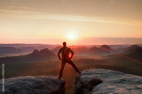 Jumping hiker in black celebrate triumph between two rocky peaks. Wonderful daybreak with sun above head..
