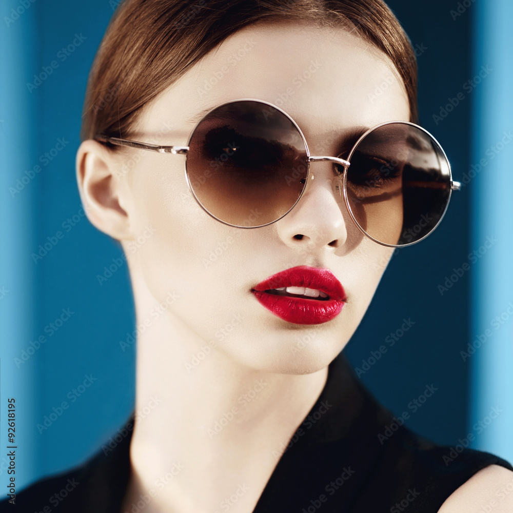 Portrait of a beautiful girl in round glasses on a blue background in studio Portrait of a beautiful girl in round glasses on a blue background in studio