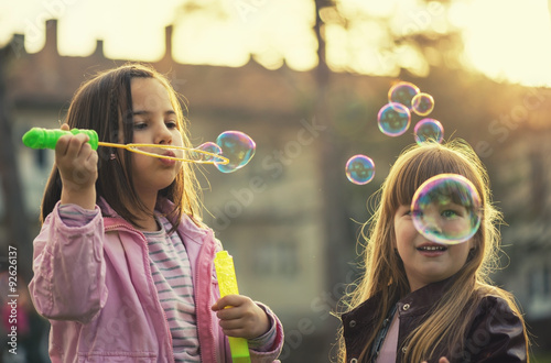 Young girls having a good time in park, blowing bubbles and smiling. Selective focus on girl on right. Old film look.