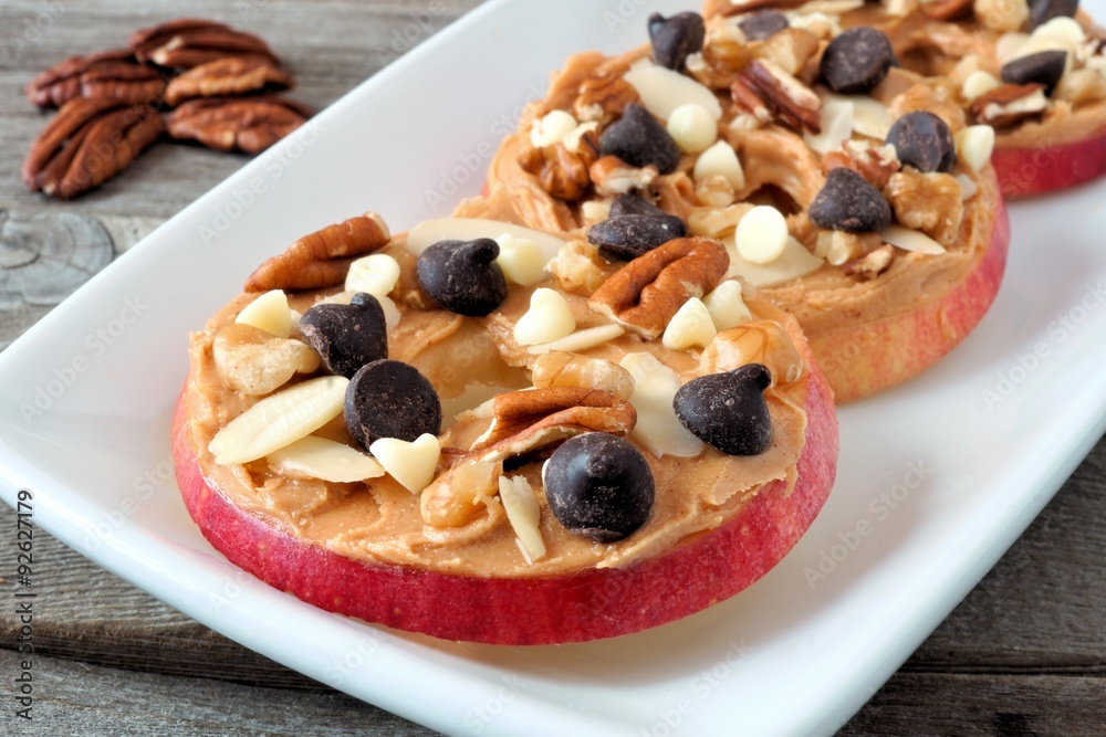 Autumn apple rounds with peanut butter, chocolate chips and nuts, on white serving plate Autumn apple rounds with peanut butter, chocolate chips and nuts, on white serving plate