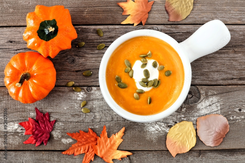 Creamy butternut squash soup topped with pumpkin seeds and cream on rustic wood background with autumn leaves