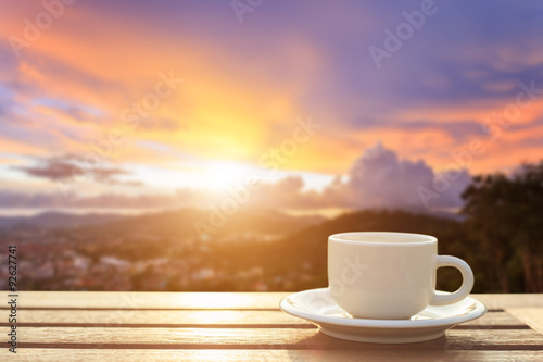 Coffee cup on wood table at sunset or sunrise time