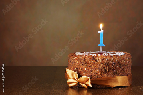 Birthday chocolate cake with burning candle as a number one on brown background