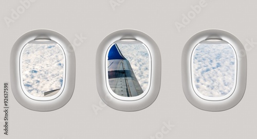 Looking out the windows of a plane to the aircraft wing and clou