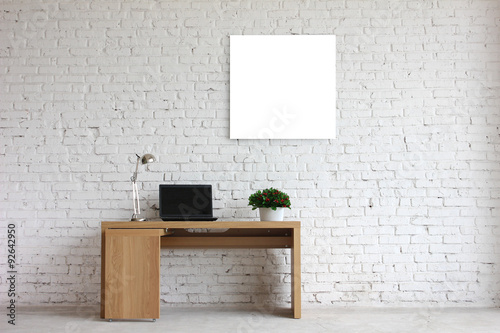an interesting example of an office interior, against the wall of white brick. office desk, laptop, flowers