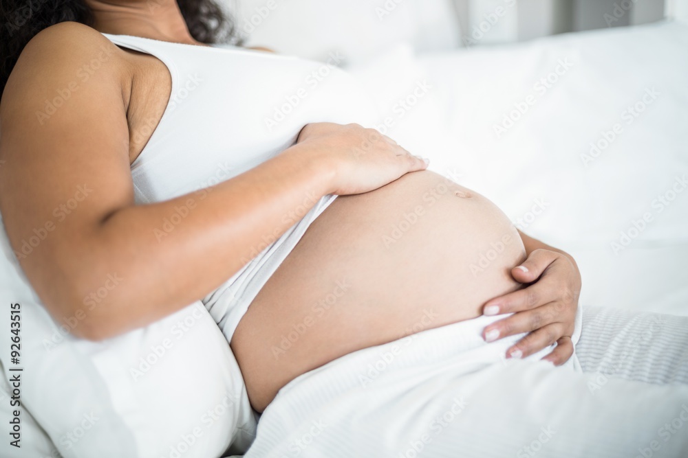 Pregnant woman embracing her belly while resting in bed Pregnant woman embracing her belly while resting in bed