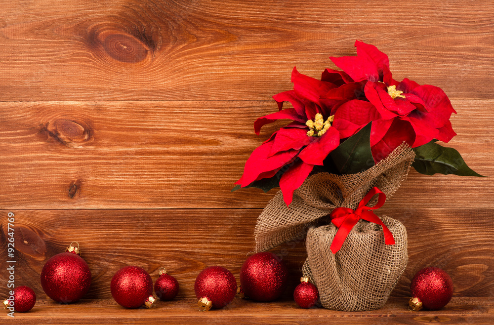 Christmas decoration - artificial red poincettia flower wrapped in sackcloth with red balls on the wooden background.