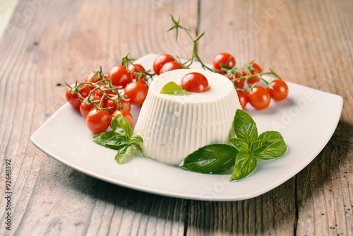 Ricotta with basil and cherry tomatoes on wooden table
