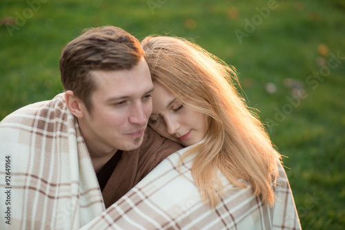 Tenderness of a young couple in the park. They are under covers.