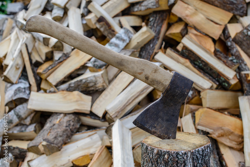 Closeup of an axe sticking in a chunk of firewood in front of a