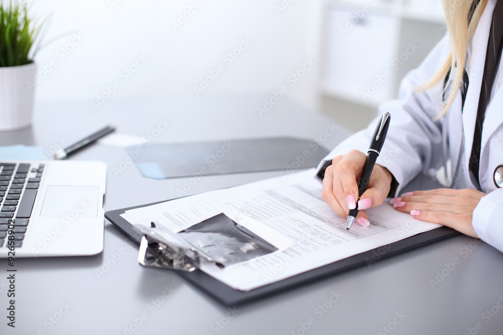Close up of female doctor filling up a medical history form, sitting at the table in hospital Close up of female doctor filling up a medical history form, sitting at the table in hospital