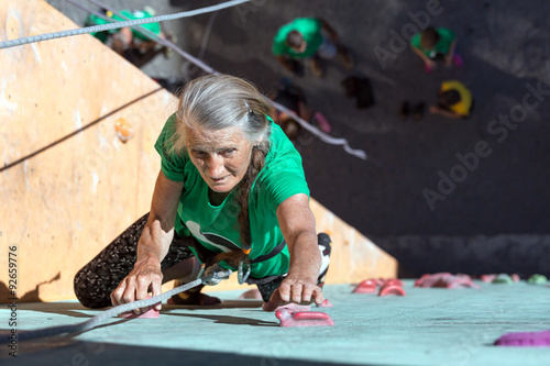 Aged Woman Climbing Wall
Elderly Female Demonstrates Excellent Physical and Moral Abilities Ascending Vertical Climbing Wall Group of Climbers Staying Below on Ground